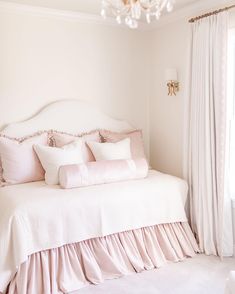 a white bed sitting in a bedroom next to a window covered in pink sheets and pillows