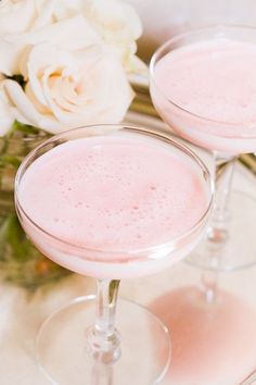 two glasses filled with pink liquid sitting on top of a table next to white flowers