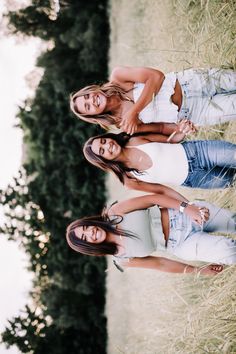 three young women standing next to each other in front of a tree and grass field