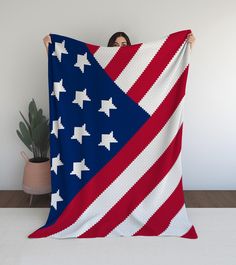 a woman is holding up a large american flag quilt in front of a potted plant