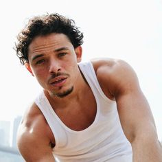 a man with curly hair wearing a white tank top