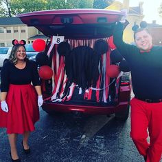 a man and woman in mickey mouse costumes standing next to a car with balloons on it