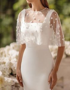 a woman wearing a white wedding dress with sheer sleeves