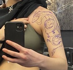 a woman with a dragon tattoo on her arm holding a cell phone in front of her