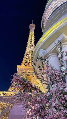 the eiffel tower lit up at night with pink flowers in front of it