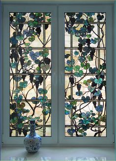 a vase sitting in front of two stained glass windows with vines and leaves on them