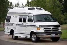 an rv is parked on the side of the road near some trees and grass in front of it