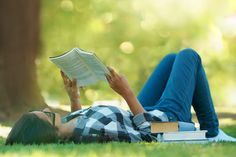 a woman laying on the grass reading a book while holding an open book in her hands