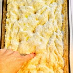 a person touching the top of a casserole in a pan with white sauce on it