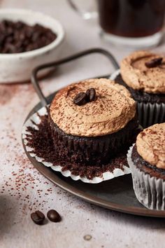 three chocolate cupcakes on a plate with coffee beans and milk in the background