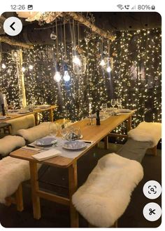 a dining room filled with lots of lights and long wooden table surrounded by white sheepskin chairs