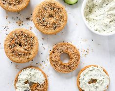 four bagels with cream cheese and sprinkles next to cucumbers