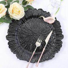 there is a black plate with two forks on it next to some flowers and wine glasses