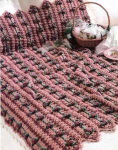 a crocheted blanket on a bed next to a basket and cup with tea in it