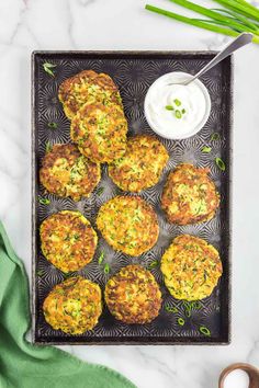 crab cakes on a tray with sour cream and green onions next to it, ready to be eaten