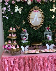 a table topped with lots of cakes and cupcakes next to a wall covered in flowers