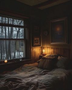 a bed in a dark room next to a window with two candles on the windowsill