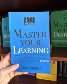 a person holding up a blue book in front of bookshelves with the title master your learning