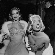 two women dressed in evening gowns and fur stolers posing for the camera with one woman