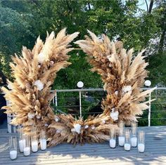 two wreaths made out of dried plants and candles on a wooden deck with trees in the background