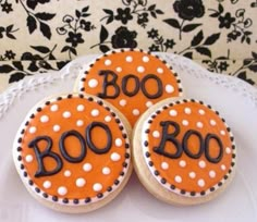 three decorated cookies sitting on top of a white cake plate with the word boo spelled out