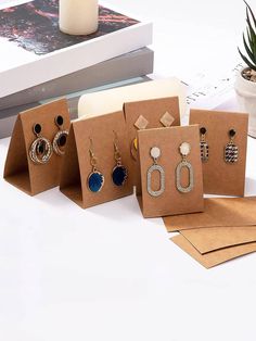 five pairs of earrings sitting on top of brown paper bags next to a plant and book