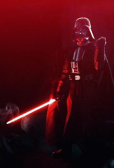 darth vader standing in the dark with his lights on and holding a light saber