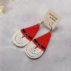 red and white beaded earrings with black accents on a gray surface next to a card