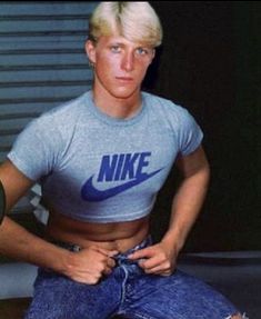 a man sitting on top of a wooden bench wearing a nike shirt and ripped jeans