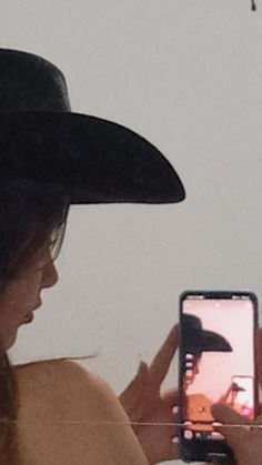 a woman wearing a cowboy hat is looking at her cell phone