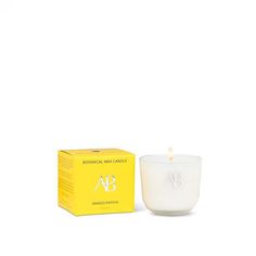 a white candle sitting next to a yellow box on a white surface with the letter ab in it