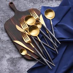 five spoons and six forks on a wooden cutting board with blue napkin next to them