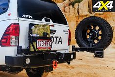 the back end of a white truck parked on top of a sandy beach next to a cliff