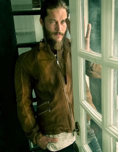 a man standing in front of a window with his hand up to the camera and wearing a brown leather jacket