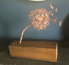 a wire plant on top of a wooden block in front of a blue painted wall