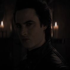 a man with dark hair and piercings wearing a black jacket in a dimly lit room