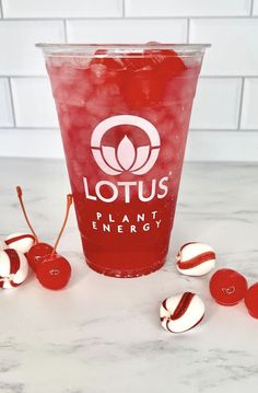 a plastic cup filled with liquid next to some cherries