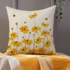 a yellow and white pillow sitting on top of a bed next to a vase filled with flowers