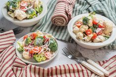 two plates with broccoli, cauliflower and tomatoes on them next to a fork