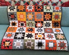 an orange and black patchwork quilt on a blue couch in front of a red wall