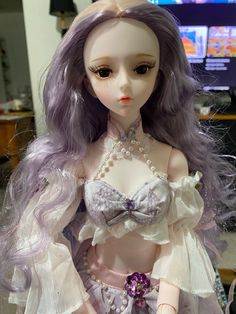 a close up of a doll with purple hair wearing a dress and pearls on it's head