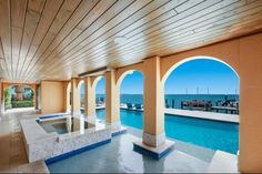 an indoor swimming pool surrounded by pillars and arches with the ocean in the background,