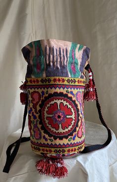 "Medium Drawstring Silk Petit Point Handbag created and handmade in Uzbekistan. Trimmed and Lined with silk and cotton ikat fabric, hand woven silk strap with tassels and a drawstring closure. Each handbag is hand drawn onto cotton canvas, inspired by original designs from Uzbekistan textile history.  8\" high x 8.5\" width(17\" in diameter), top opening 17\" wide, approx. 57\" strap x 3/4\" width. Drawstring goes through ikat channel and has tassels at the opening of the channel. Fits largest s Textile History, Handmade Fabric Bags, Handmade Rakhi, Embroidered Handbag, Medium Handbags, Carpet Bag, Drawstring Bucket Bag, Thread Jewellery, Festival Bag