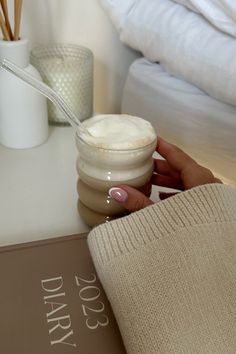 a person is holding a spoon over a jar of cream on a table next to a book