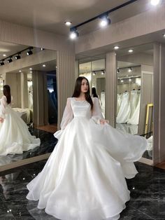 a woman standing in front of a mirror wearing a white wedding dress with long sleeves