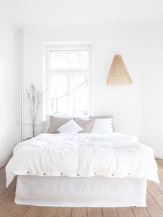 a bed with white linens and pillows in a bedroom next to a large window