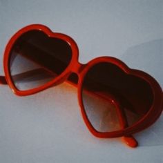 a pair of red heart shaped sunglasses sitting on top of a white surface with an orange handle