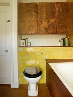 a white toilet sitting inside of a bathroom next to a wooden cabinet and counter top