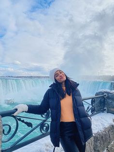 a woman standing in front of a waterfall with snow on the ground and water behind her