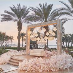 an outdoor wedding setup with chandeliers and pink flowers on the ground, surrounded by palm trees